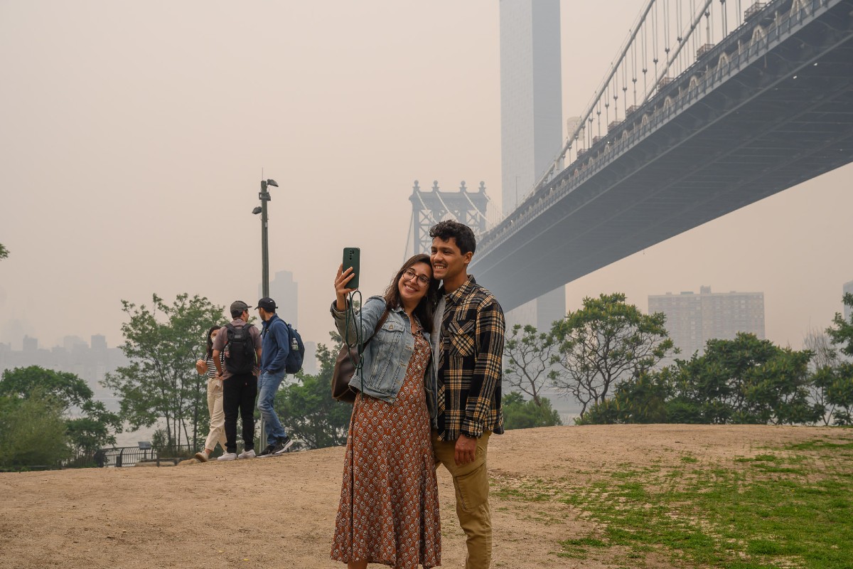 Two people take a selfie in front of the Brooklyn Bridge on June 7, 2023.