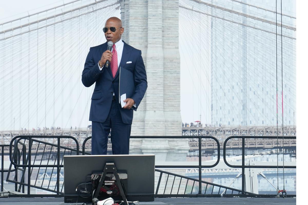Eric Adams in sunglasses in front of the Brooklyn Bridge