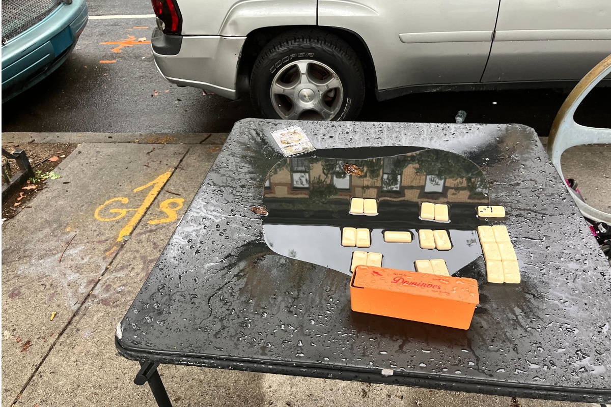 Dominos on a soggy black card table, on a NYC sidewalk.