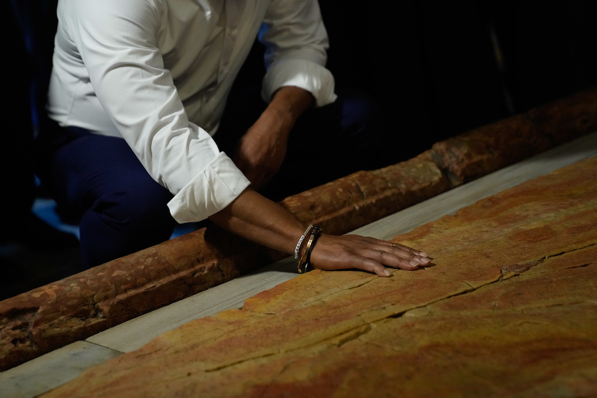Mayor Eric Adams in a white button-down and bracelets around his wrist, touching a stone slab.
