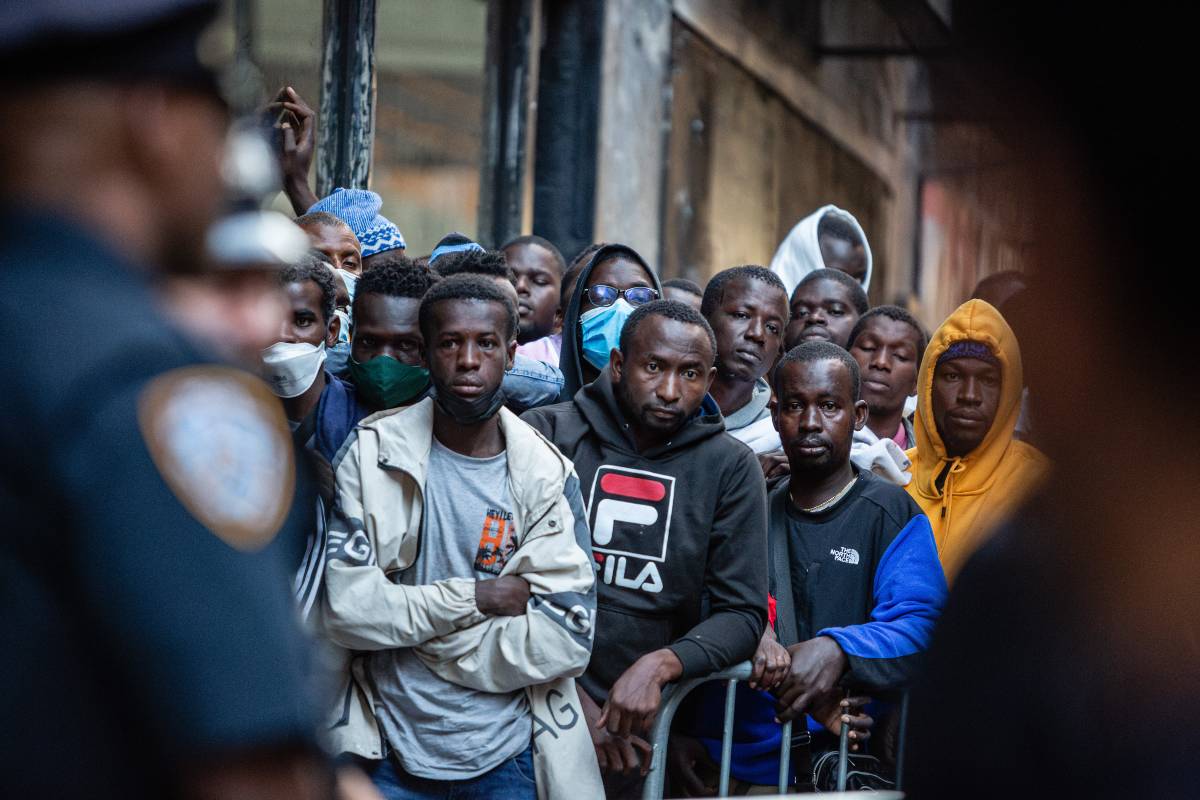 Asylum-seekers wait outside the Roosevelt Hotel as police look on