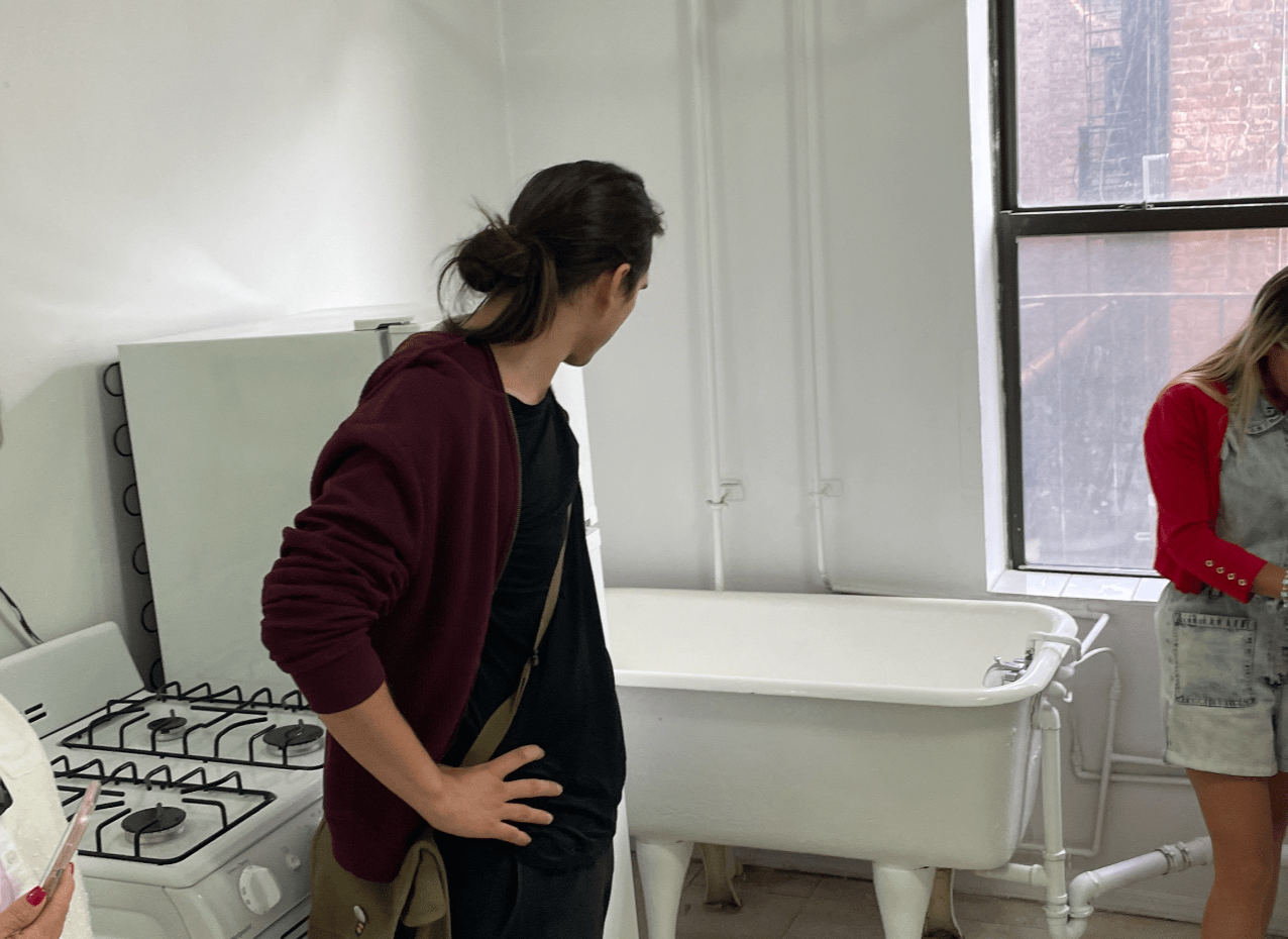 A prospective tenant assesses a bathtub in the kitchen of a studio apartment.