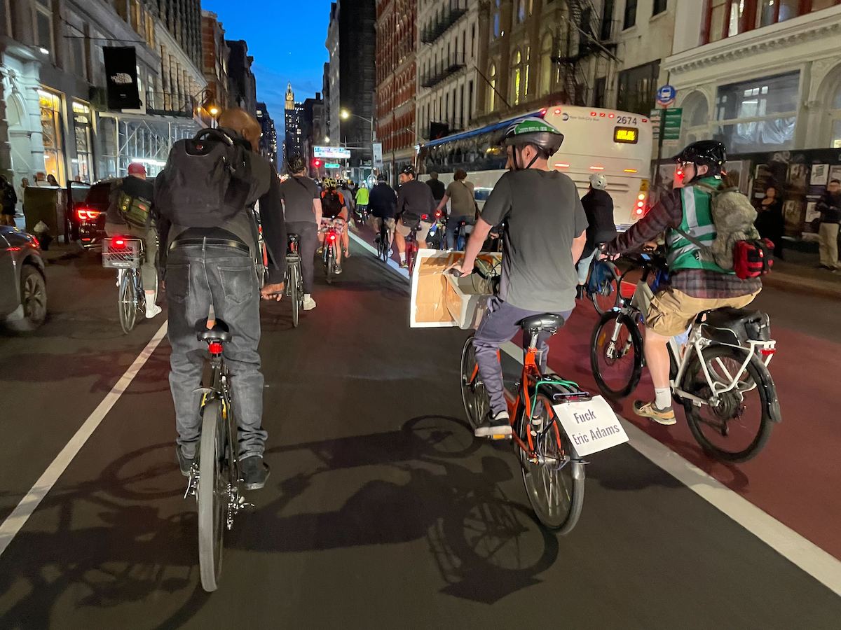Cyclists ride down Broadway to protest a record number of cyclings deaths. One has a sign on the back of his bike that says "Fuck Eric Adams"