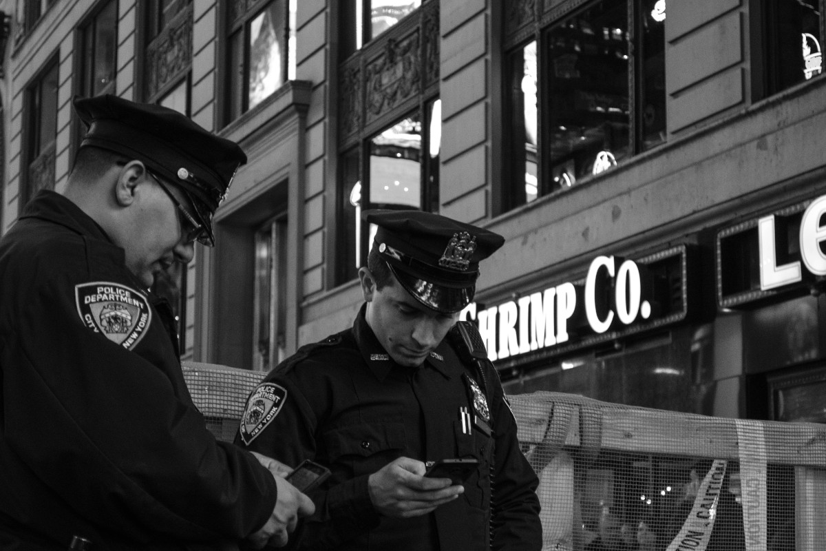 Two NYPD officers look at their phones near a store.