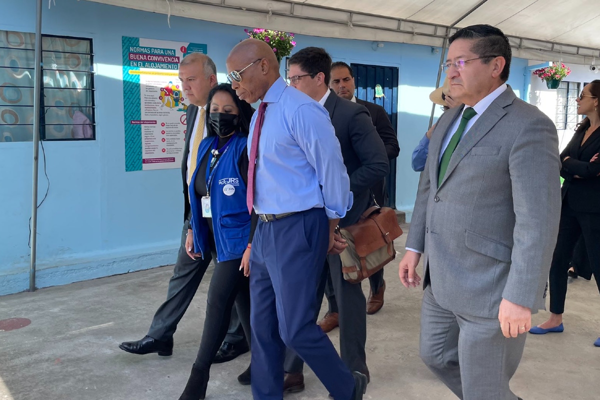 Eric Adams in aviator sunglasses and business attire walks with his hands behind his back with a group of people