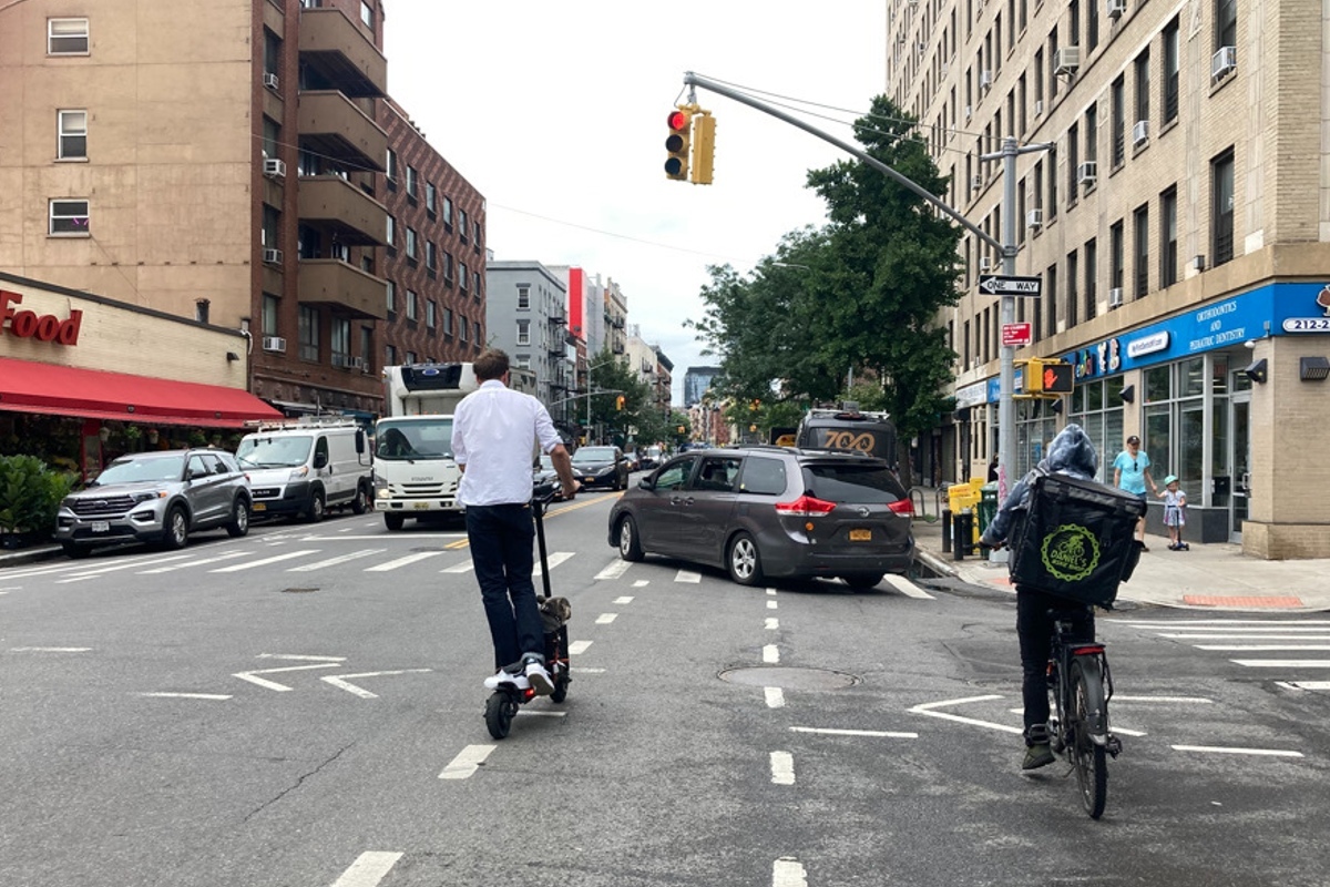 A guy on a stand-up scooter and an e-bike delivery rider navigate a bike lane in the East Village.