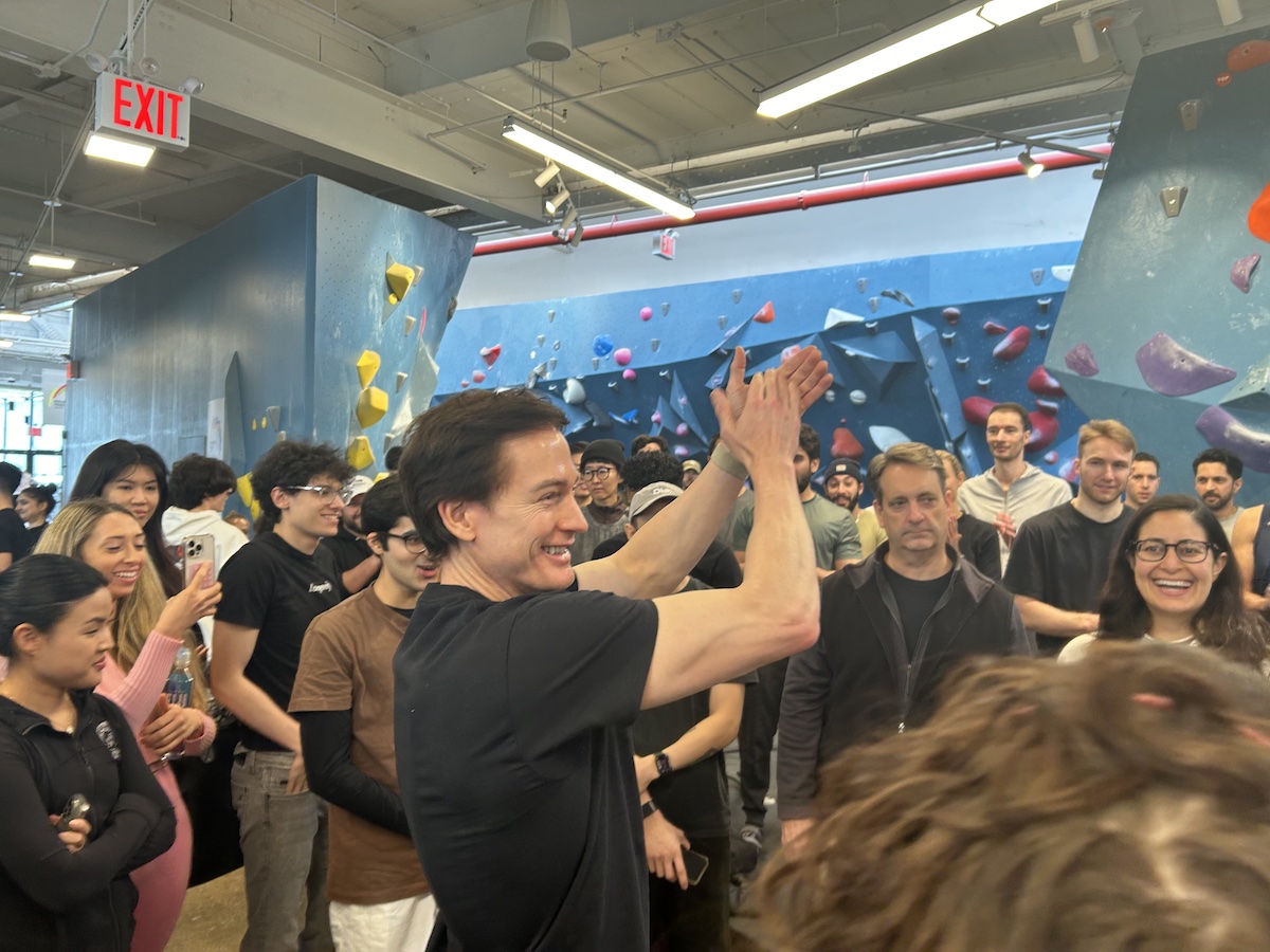 Brian Johnson raises his hands up in the air while speaking to a crowd at a Brooklyn climbing gym.