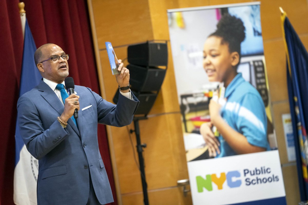 DOE Chancellor David Banks speaks at an event next to a banner bearing the new NYC Public Schools name.