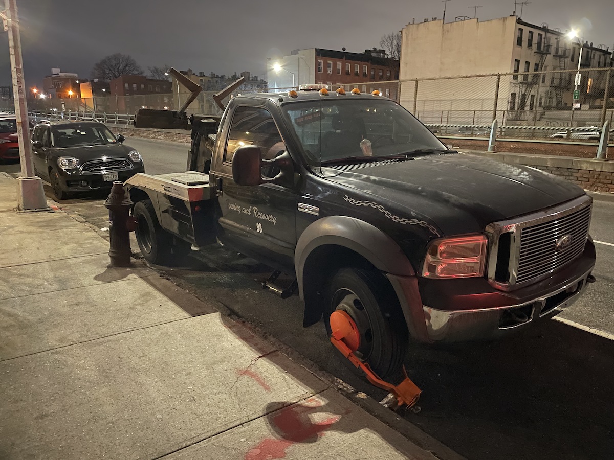 A tow truck with a boot on the wheel parked in front of a fire hydrant.