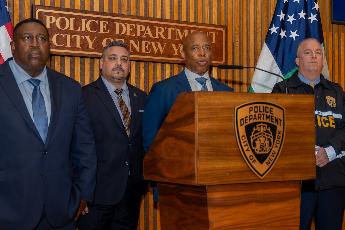 Mayor Adams stands at a podium at NYPD headquarters surrounded by his police leadership.