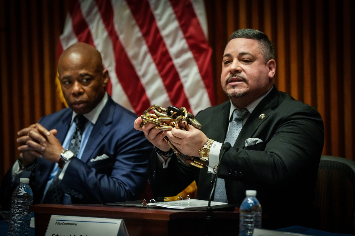 NYPD Commissioner Edward Caban holds up a bike lock during a press conference while sitting next to Mayor Eric Adams.